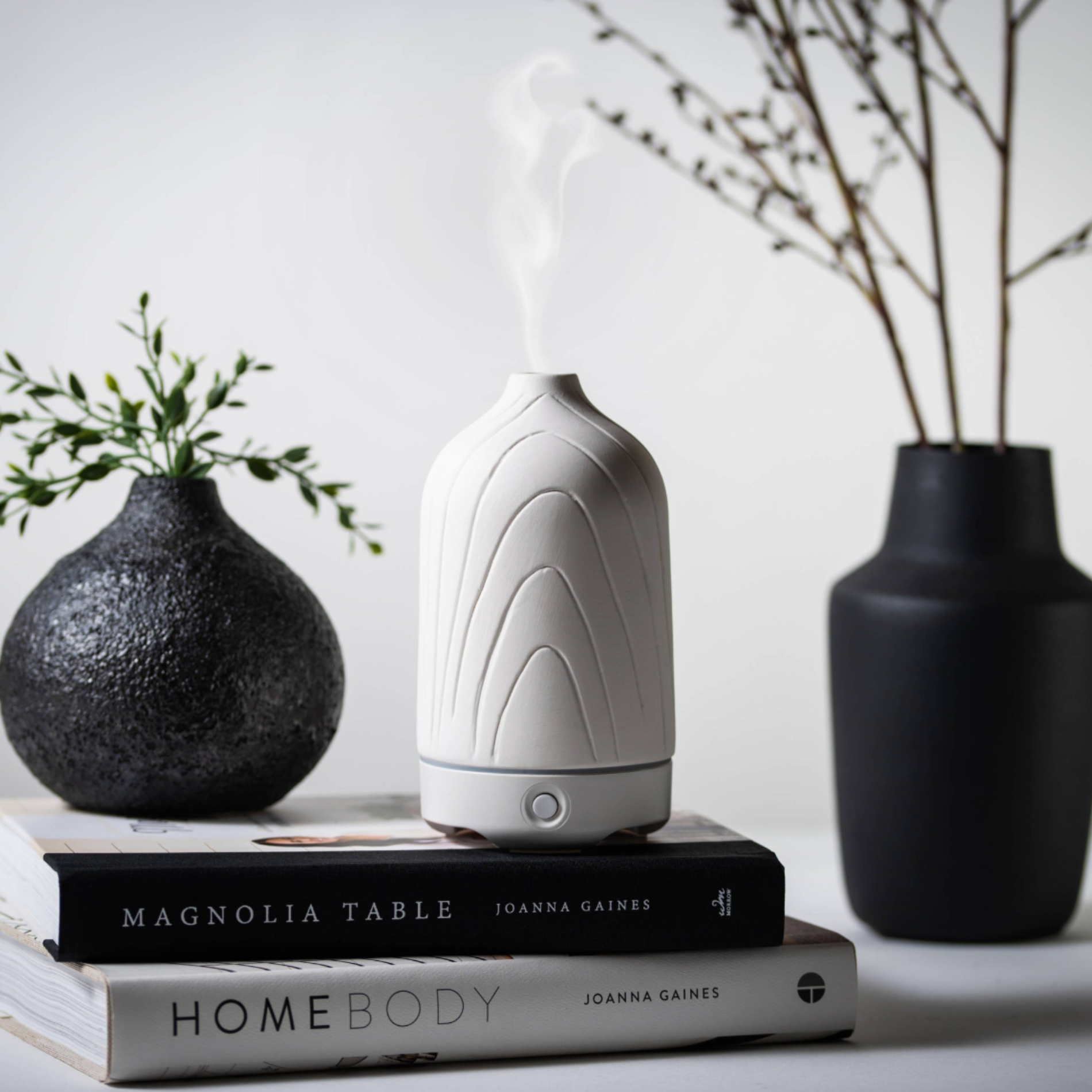 White diffuser on books with decorative vases and plants in the background